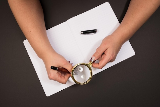 A close-up of a person's hand holding a magnifying glass over a document with official stamps and signatures. The focus is on the details of the document and the hand holding the magnifying glass.