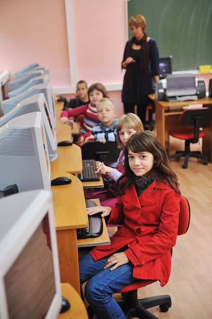 A teacher is explaining a lesson to students in a computer classroom. The classroom is filled with focused students on their laptops.