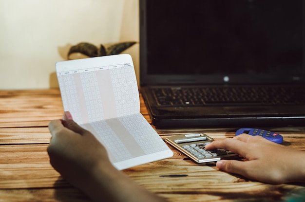A close-up shot of a hand holding a calculator over a spreadsheet filled with financial data and tax calculations. The focus is on the calculator screen displaying a final tax amount.