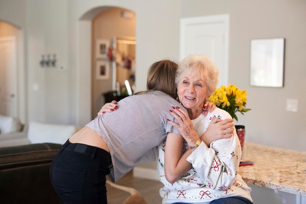 A caregiver joyfully embraces an elderly woman in her home. They both are smiling and comfortable; the scene is filled with warm, soft light. This represents happy domestic care and reflects the benefits of thoughtful employee management.