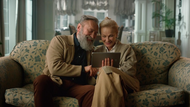 An elderly couple sitting comfortably in their living room, reviewing their financial portfolio on a tablet, with a warm and inviting atmosphere.
