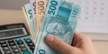 Mão segurando notas de Real com calculadora e calendário 2026 ao fundo, simbolizando o novo salário mínimo.