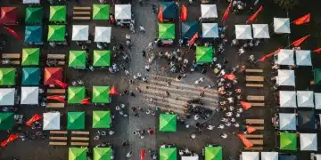 An aerial drone view of a vibrant community festival with colorful market stalls and a diverse crowd, illustrating social connection and local economic activity.