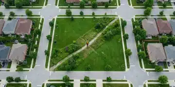 Aerial view of a modern suburban community with a person walking on a hidden path through a park, symbolizing discovery of overlooked resources.